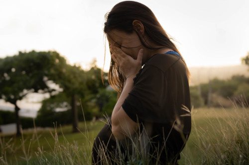 A sad pregnant woman sitting outside in a field crying 