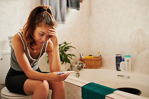 Young woman looking at her positive pregnancy test and wondering is adoption right for me