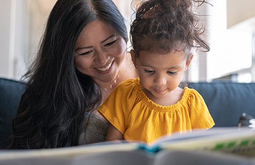 Adorable toddler being read a book by her adoptive mother