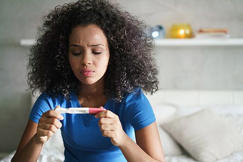 Woman sits on her bed with a positive pregnancy test and thinks about giving baby up for adoption