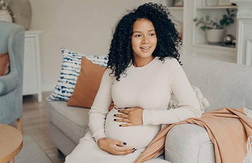 Young pregnant woman seated in her living room and cradling her belly