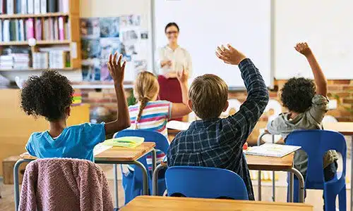 Children in a classroom raising their hands to answer a question