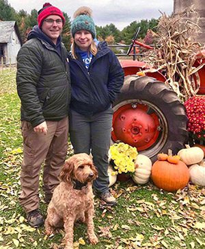 Cody and Harlie pose with their Goldendoodle Mango by an autumn scene