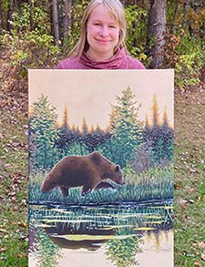 Harlie shows off one of her finished paintings of a bear walking by a pond