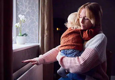 Woman struggling with single mom pregnancy and trying to stay warm by radiator at her apartment
