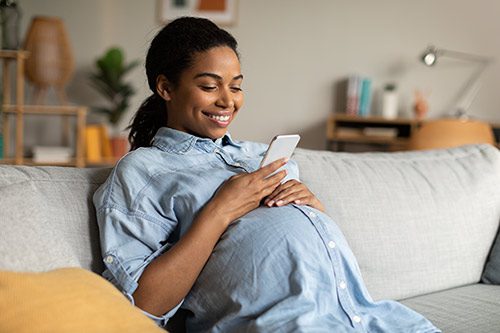 Pregnant African American woman in her living room, looking at an adoption app on her phone