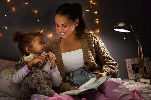 Happy adoptive mother and her daughter smile at each other while reading children's books about adoption