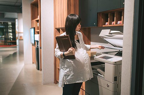 Pregnant woman making copies while struggling to work whil pregnant