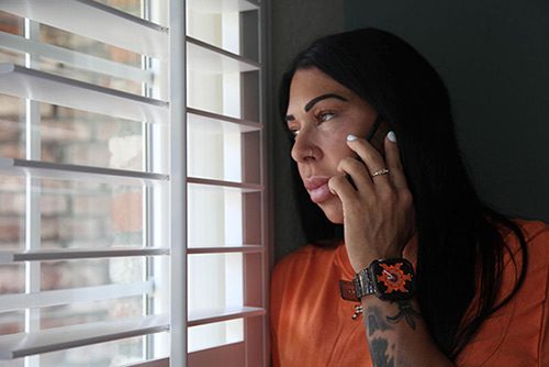 Hispanic woman looking out her living room window while talking on her cell phone