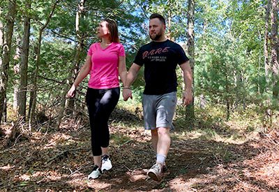 Jill and Chris holding hands while taking a scenic hike through the woods