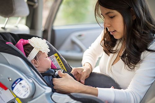 Adoptive mother carefully buckles her newborn daughter into her carseat