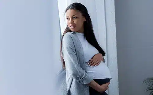 pregnant woman touching her belly while looking at window 