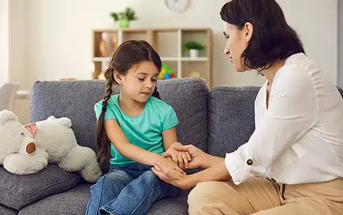 Adoptive mother sitting with daughter, holding her hands, talking to her about her adoption