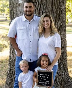 Adoptive parents Noah and Kelsey with their children and an adoption letter board