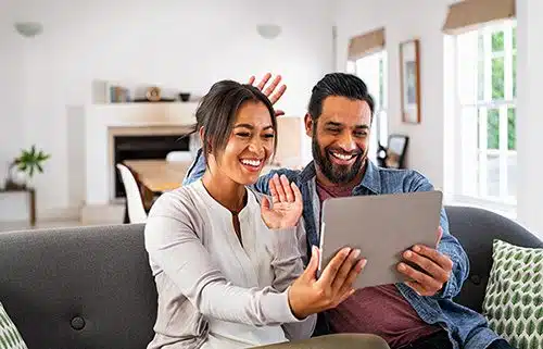 Happy couple in their living room using a tablet to make adoption announcements to family and friends