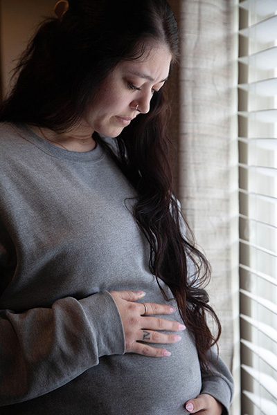 Pregnant woman pauses from looking out the window to look at her growing belly and baby