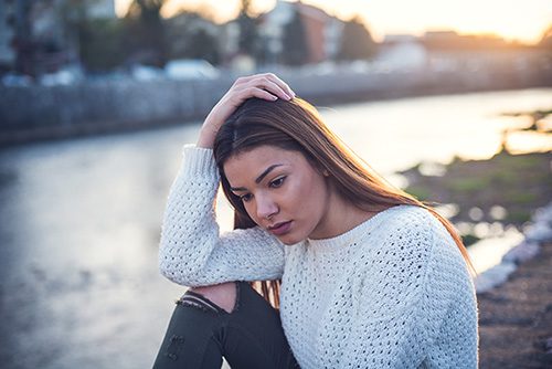 Depressed woman seated by a river in the city