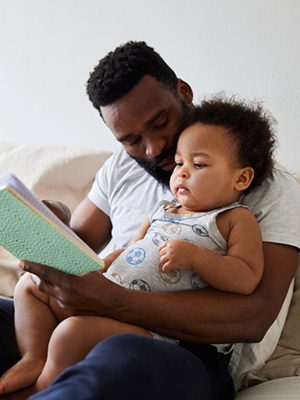 Adoptive father reading to his toddler son in bed