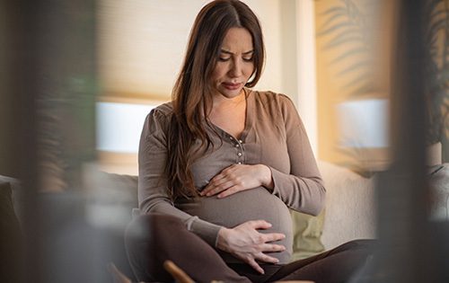 Pregnant woman sitting cross-legged and massaging her belly with anxiety