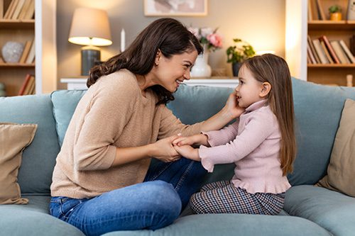 An adoptive mother chats with her young daughter on the sofa