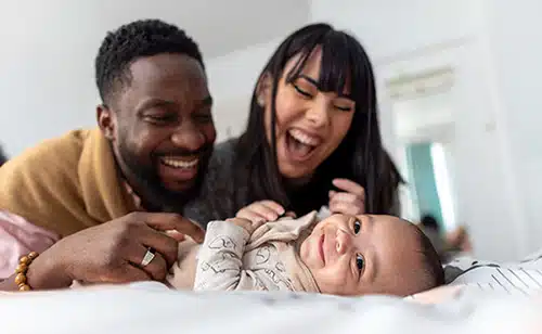 Happy adoptive couple playing with their infant son at home