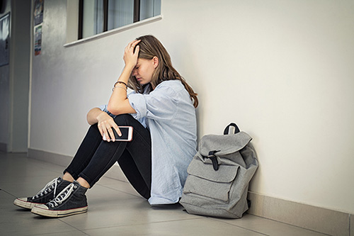 Upset teen girl at school seated in a hallway