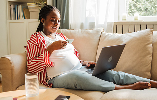 Black woman holding a credit card as she shops for affordable maternity clothing online