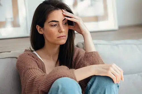 Depressed young woman thinking about her problems while sitting on the sofa at home
