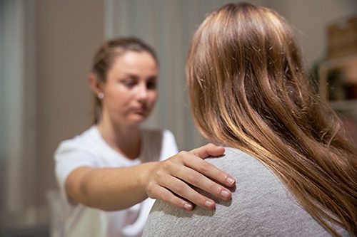 Closeup of a woman's helping hand on her friend's shoulder