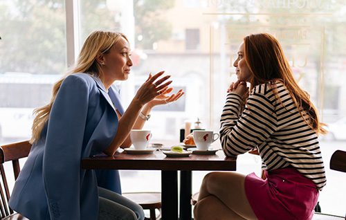 Two female friends talking while seated at a table at a coffee shop