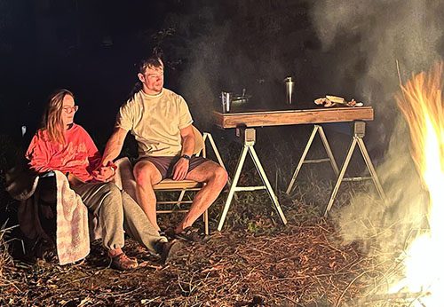 Maggie and Blake holding hands while watching a bonfire 