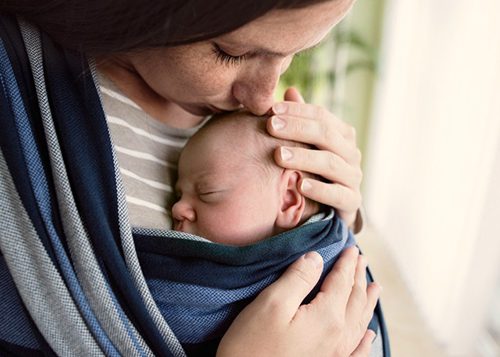 Adoptive mother  kissing her newborn baby son in sling at home