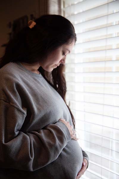 Pregnant woman near window looking at belly