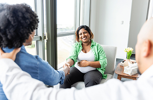 Pregnant woman smiles and shakes hands with adoptive couple