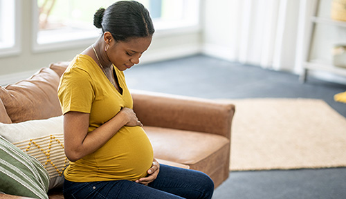 African American woman seated on sofa as she cradles her belly with her hands