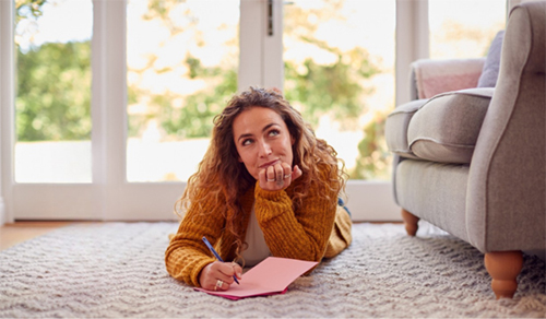 Young woman laying on her living room floor, thinking about what to write in a card