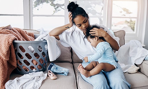 Young woman sitting on the sofa in her living room and comforting her daughter