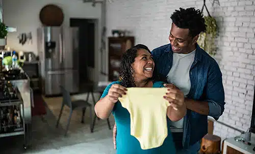 Happy couple in their kitchen, admiring a baby onesie