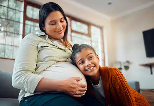 Pregnant mother with child listening to movement of baby in belly with happy smile