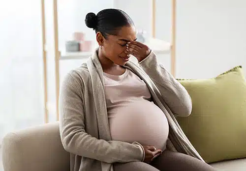 Young pregnant African American woman sitting on couch, touching her tummy 