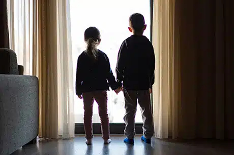 Brother and sister holding hands while looking through a window