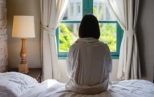 Woman sitting on her bed looking out at the window in the morning