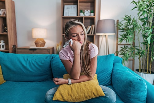 Sad young woman crying on her sofa at home 