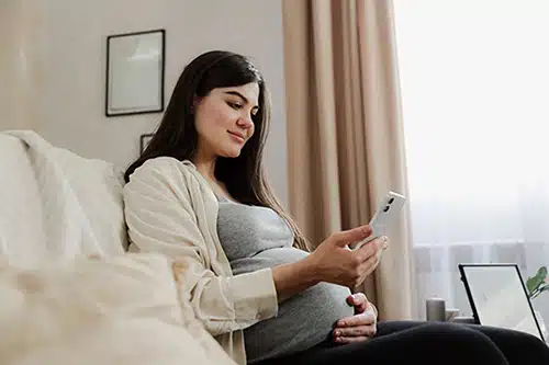 Young pregnant woman in her living room using her cell phone