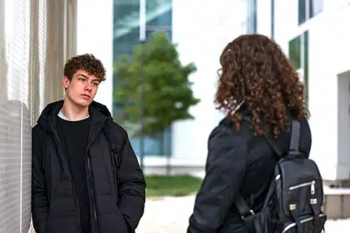 Rear view of young woman in black talking with young man on the street, leaning on the wall