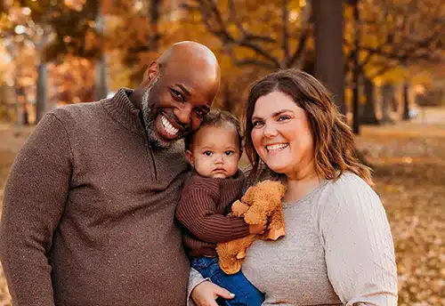 Happy couple posed outside with the baby girl they adopted through Lifetime Adoption
