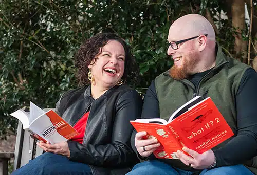 Mary and Adam laughing on a park bench while holding books