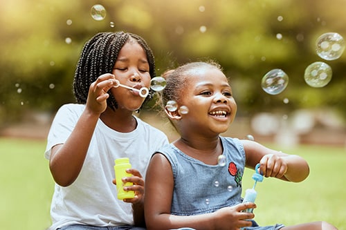 Happy adopted girl blowing bubbles at a park with her birth sibling