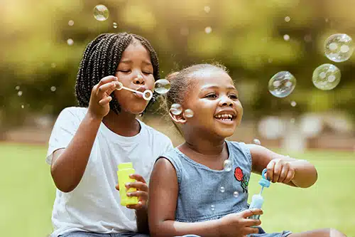 Happy adopted girl blowing bubbles at a park with her birth sibling
