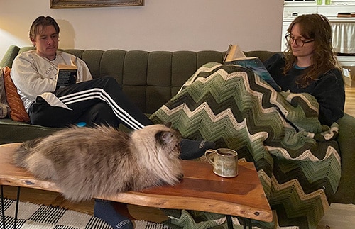 Corbin and Paige reading together in their living room while their cat rests of the coffee table